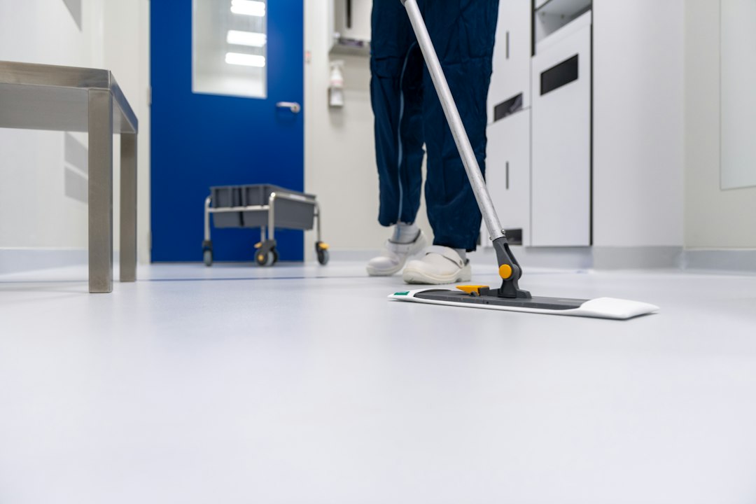 A person in blue scrubs mopping a white floor in a clinical hallway in Allen, TX
